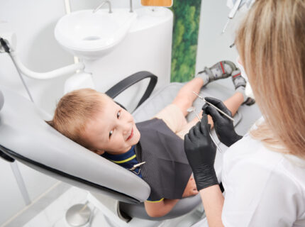 Cheerful little boy sitting in dental chair in dental office.