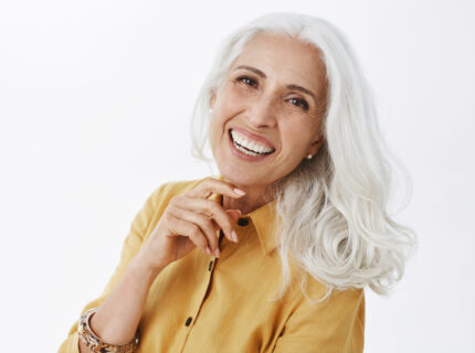 Close-up shot of happy delighted and accomplished charming european elderly female with white hair in yellow trench coat touching face gently laughing from joy feeling pretty and energized